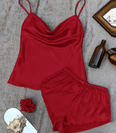 Red satin camisole and shorts set on a textured surface with decorative items.