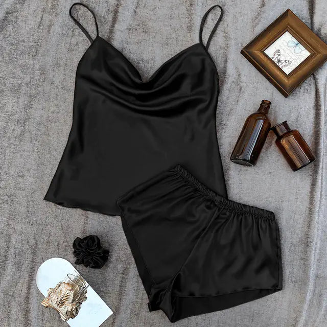 Black satin camisole and shorts set on a textured surface with decorative items.