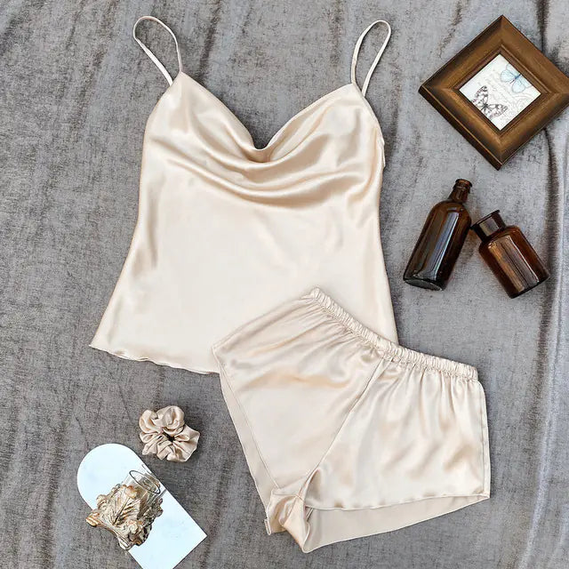 Beige satin camisole and shorts set on a textured surface with small items around.