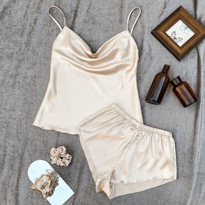 Beige satin camisole and shorts set on a textured surface with small items around.