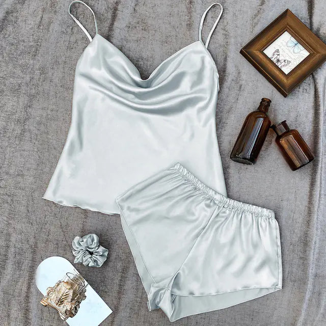 Light grey satin camisole and shorts set on a textured surface with bottles and a scrunchie.