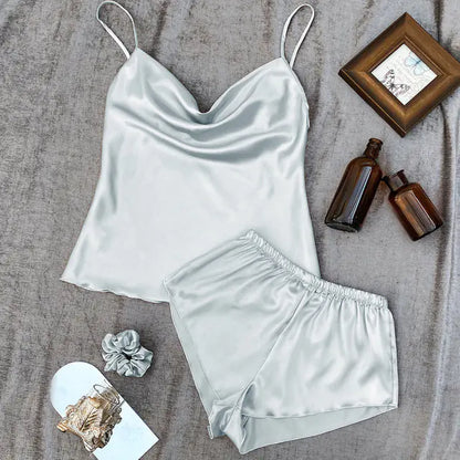 Light grey satin camisole and shorts set on a textured surface with bottles and a scrunchie.