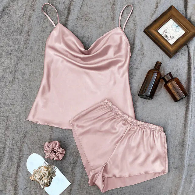 Pink satin pajama set on a textured surface with decorative items.