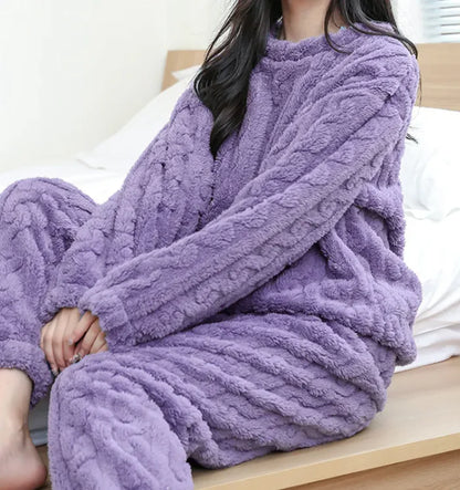 Person wearing a cozy purple cable knit sweater and matching pants on a bed.