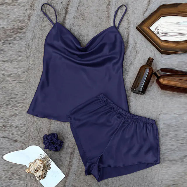 Navy blue satin camisole and shorts set on a textured surface with decorative items.